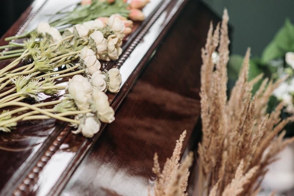 A floral arrangement featuring white roses and small pale pink flowers with green stems, arranged in a horizontal bouquet style on a polished dark wooden surface. The flowers are fresh, with delicate