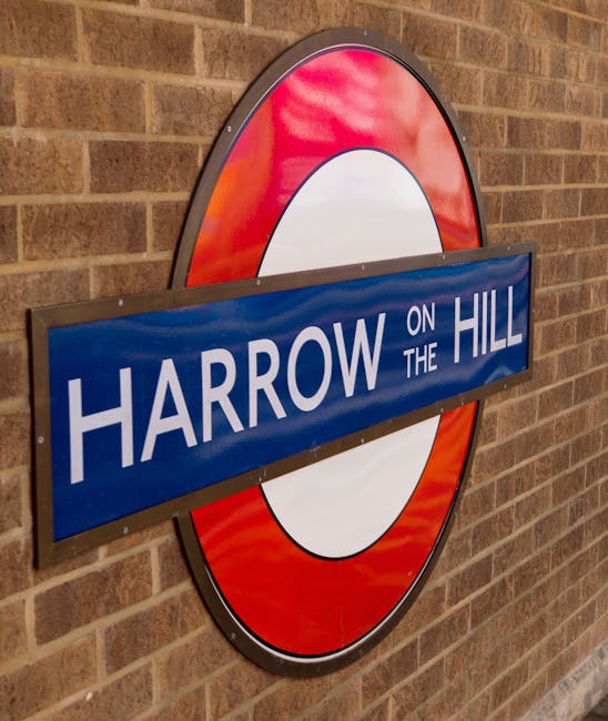 The image displays a large, circular London Underground style sign mounted on a brick wall, featuring a red outer ring and a white center. Overlaid on the sign is a blue rectangular plaque with white 