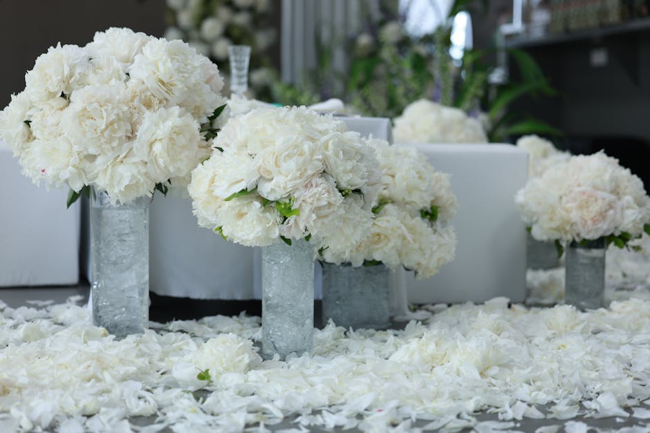 A floral arrangement featuring large, white hydrangea bouquets placed in tall, cylindrical glass vases with a frosted finish. The bouquets are lush and full, with delicate, tightly clustered petals an