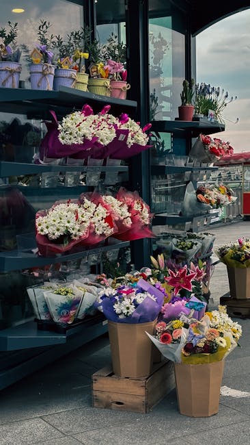 An outdoor display of floral arrangements and bouquets at a flower shop showcasing a variety of fresh flowers, including white daisies, pink lilies, and purple chrysanthemums, wrapped in colorful pape